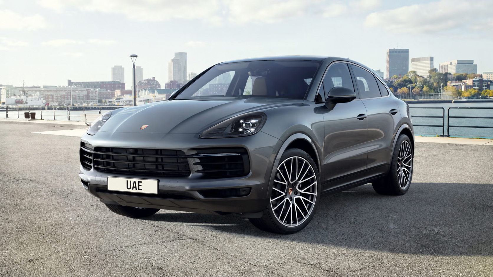 Grey Porsche Cayenne beside the waterfront with its Porsche badge visible